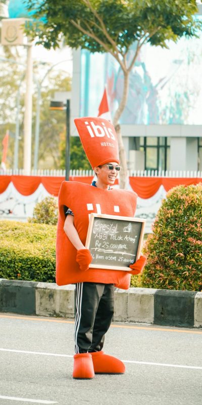 Photo by Rendi iD Person wearing a red costume holding a sign promoting a restaurant offer on a street.