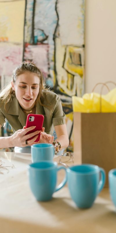 Woman using smartphone surrounded by cups and bag, ideal for online business themes.